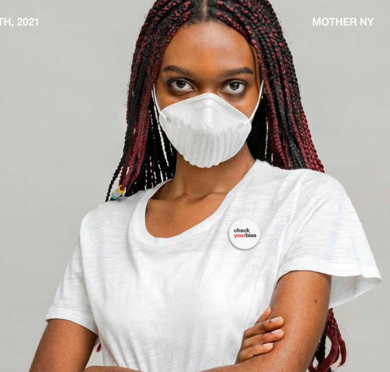 Young person with long braids and a white t-shirt wears a small pin badge reading 'check your bias'